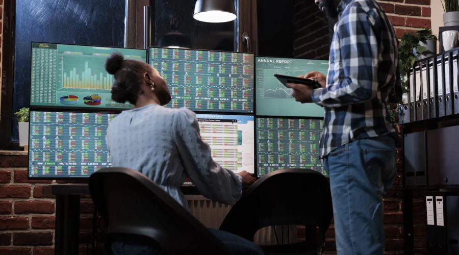 Financial analysts near multi monitor workstation using tablet device to analyze capital profit risks. Hedge fund company professional agents in office, reviewing trading strategies to take profits.